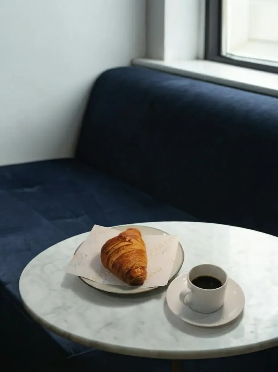 A croissant and an espresso on a marble table by the window